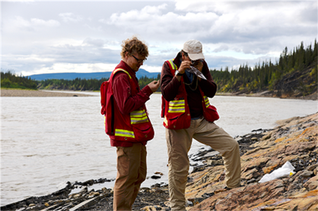Photo de deux membres du personnel hautement qualifiés observant des formations de roche en bordure d’un lac.