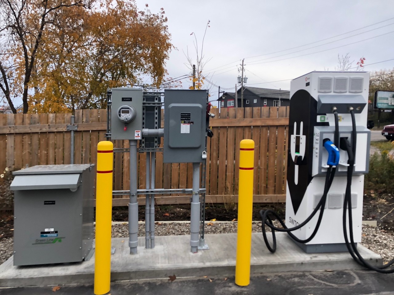 Station de recharge pour véhicules électriques située dans un terrain de stationnement devant une clôture.