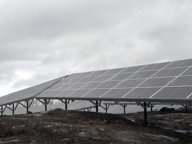 Plusieurs rangées de groupements de panneaux solaires installés sur un terrain rocheux au relief accidenté.