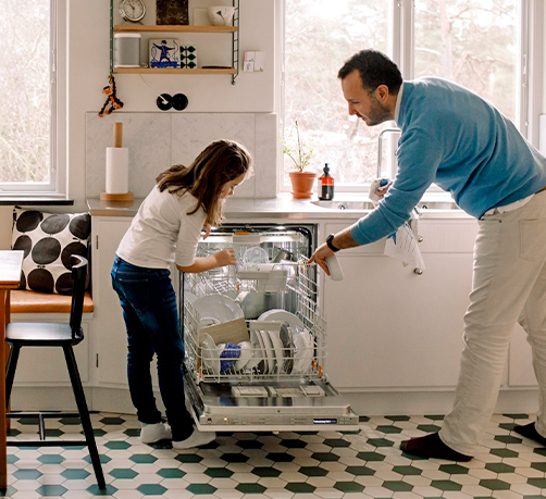 Parent et enfant arrangeant les ustensiles dans le lave-vaisselle en se tenant debout dans la cuisine.