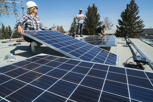 Deux ouvriers portant un casque de sécurité installent des panneaux solaires sur le toit d'une maison.