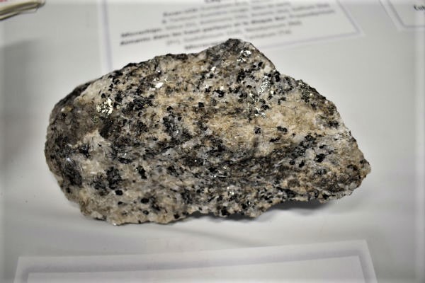 Petite roche multicolore posée sur un morceau de papier. La roche est un échantillon de carbonatite avec du niobium et des ETR provenant d’Oka (Québec).