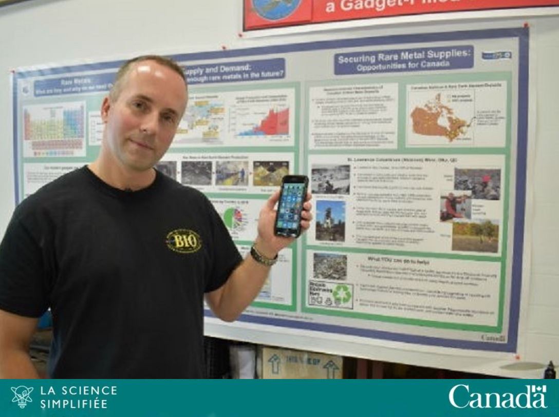 Michael Parsons, chercheur scientifique à RNCan, se tient devant un panneau d’affichage avec un téléphone portable dans sa main gauche.