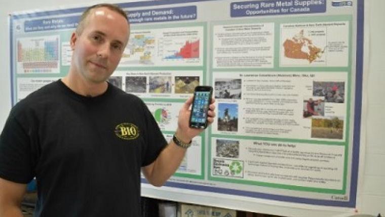 Michael Parsons, chercheur scientifique à RNCan, se tient devant un panneau d’affichage avec un téléphone portable dans sa main gauche.