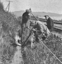 Techniciens qui prennent des mesures avec un cheminement de précision dans un fossé sur le côté d'un chemin de fer.