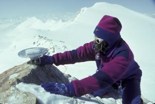 Technicien sur une cime neigeuse dans vêtement d'hiver qui tient une antenne GPS avec un fond montagneux