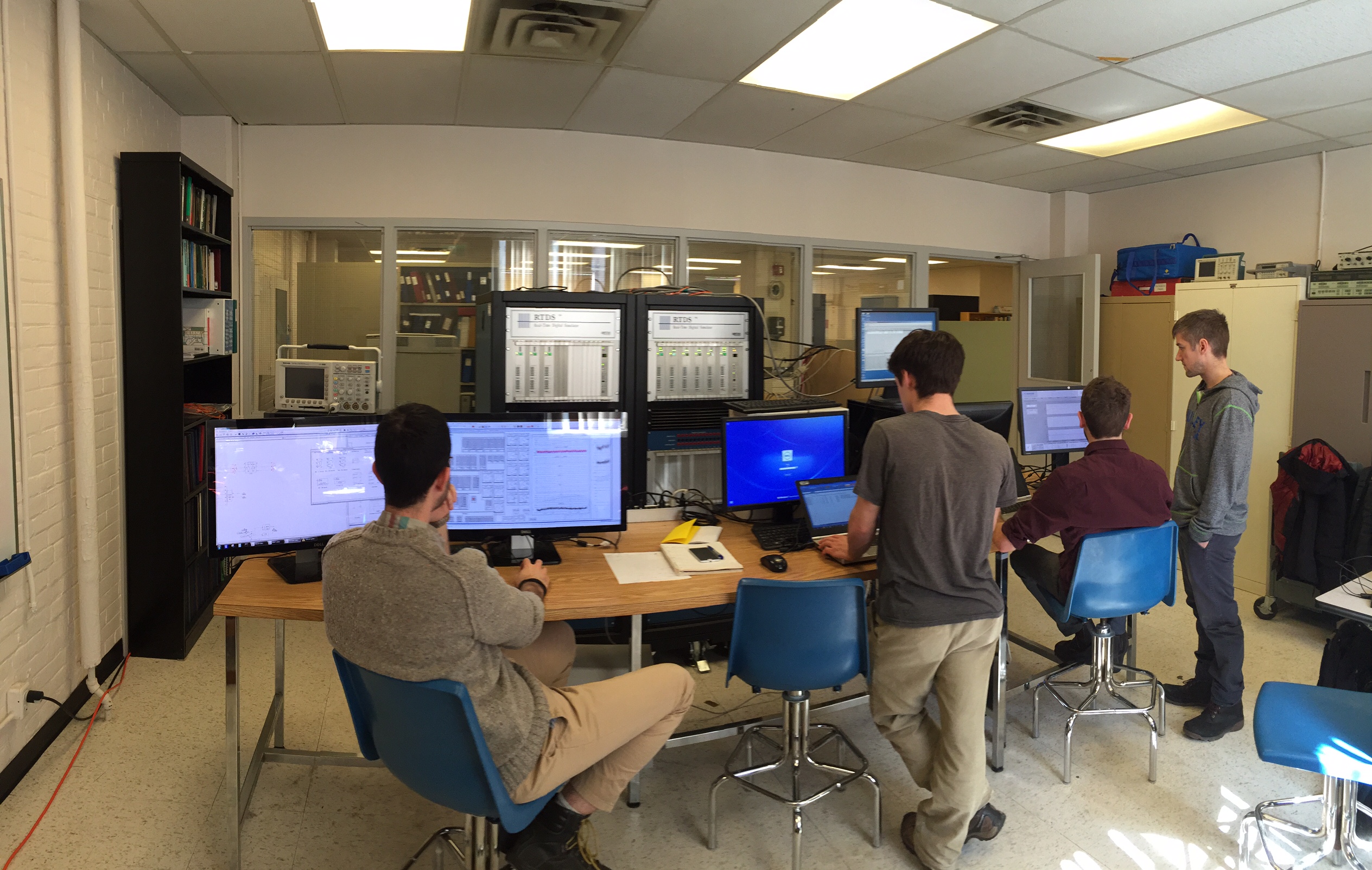 La photographie montre l’environnement de l’installation de mise à l’essai, avec quatre ingénieurs de Hatch qui travaillent à des terminaux d’ordinateur branchés à un simulateur en temps réel et au matériel de contrôle d’un microréseau