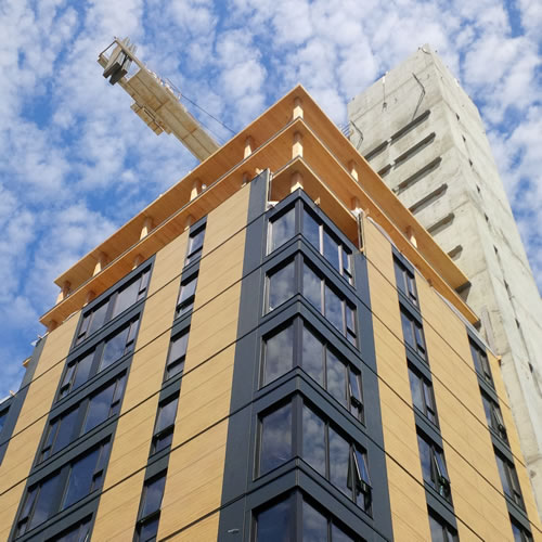Un bâtiment de grande hauteur hybride en bois massif de 18 étages durant les stages finaux de construction. Les fenêtres et revêtement ont finis partiellement et les planchers en bois et une colonne en béton sont dévoilés.